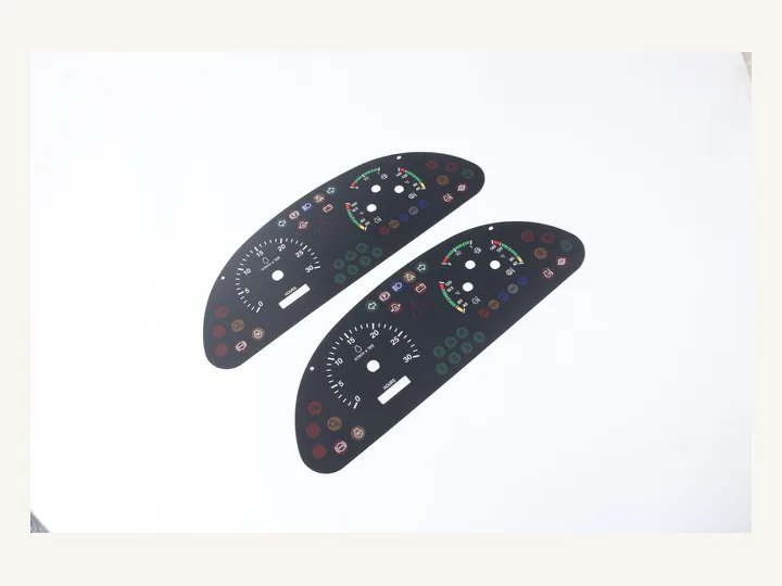 Two printed automotive dashboard overlays with gauge openings and indicator icons